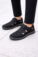 Black sandals worn with black pants on a light gray floor.